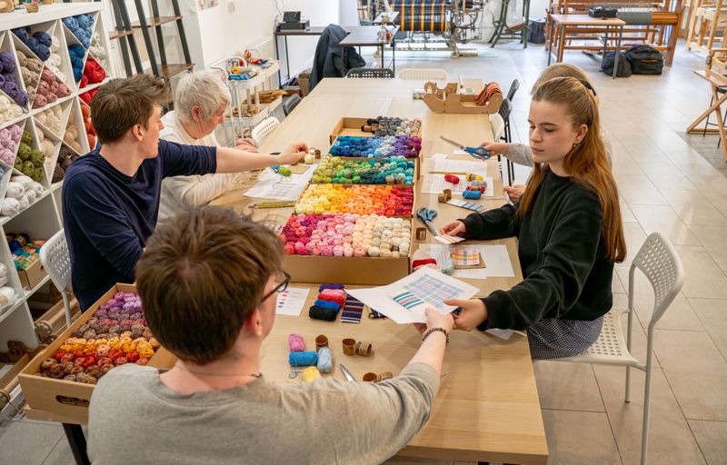 A group of people working with fabric and yarns around a table.