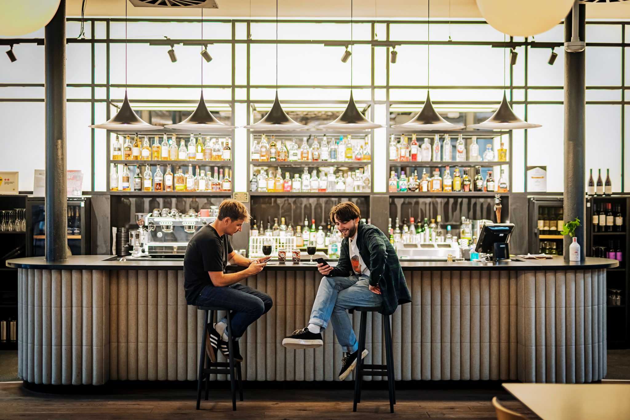 A broad shot of two men sitting at a bar with lots of fancy bottles