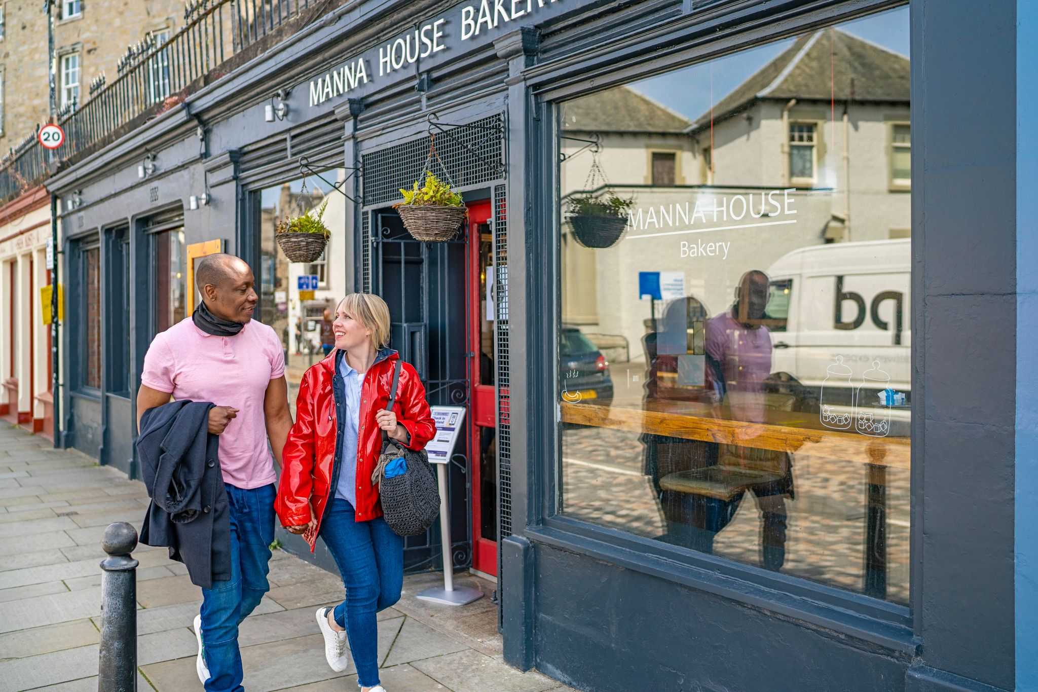 A man and a woman walking down a high street outside of a bakery