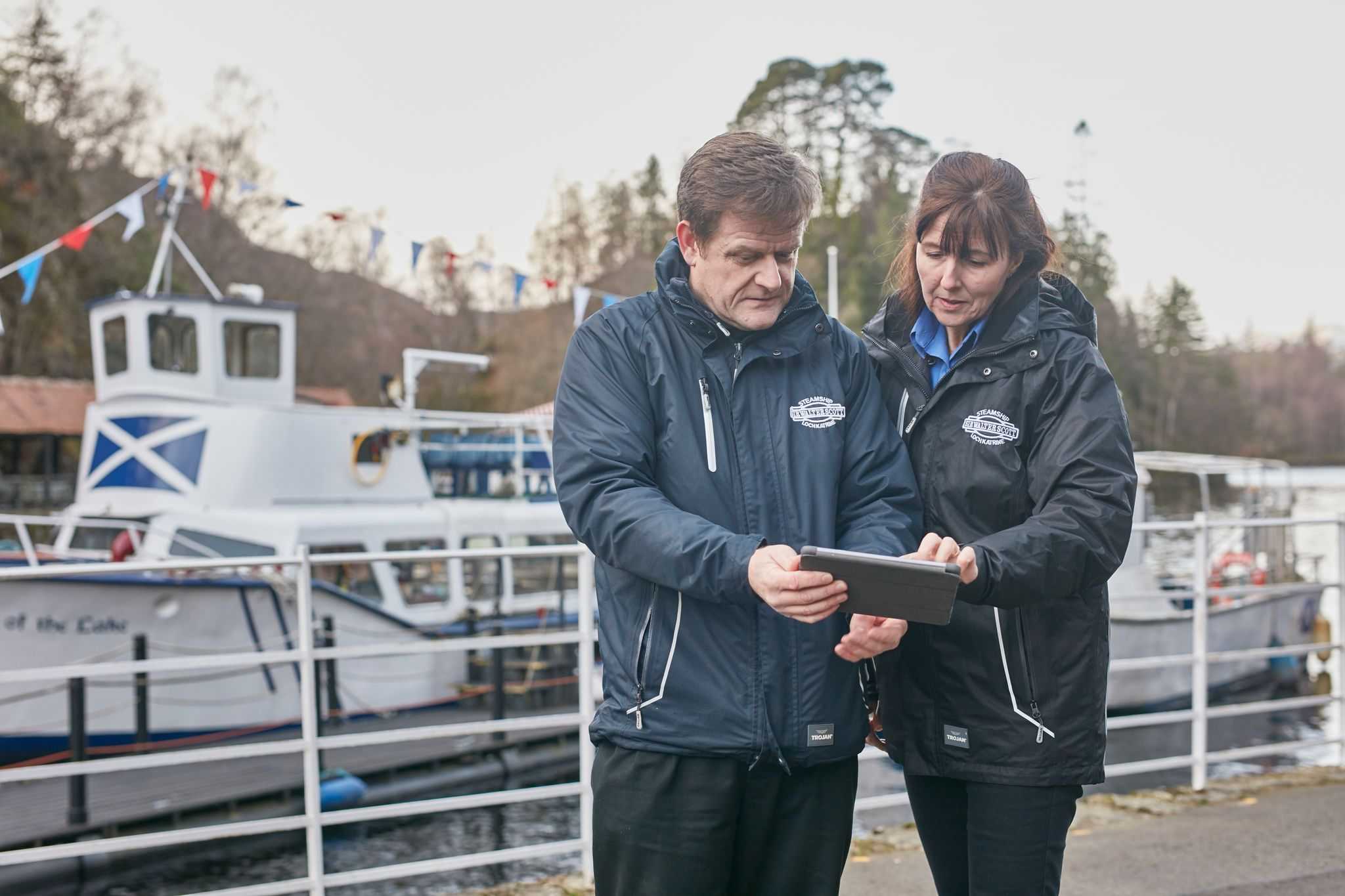 Man and woman using tablet by shore of loch