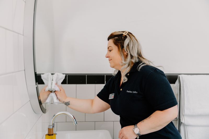 A member of housekeeping cleaning a bathroom mirror