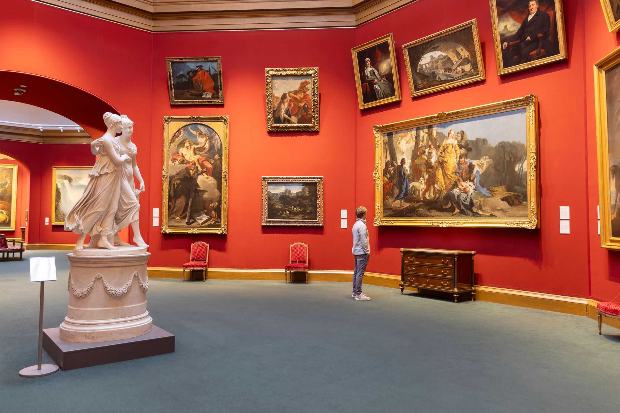 Person looks at paining in a a large gallery with statue in foreground.