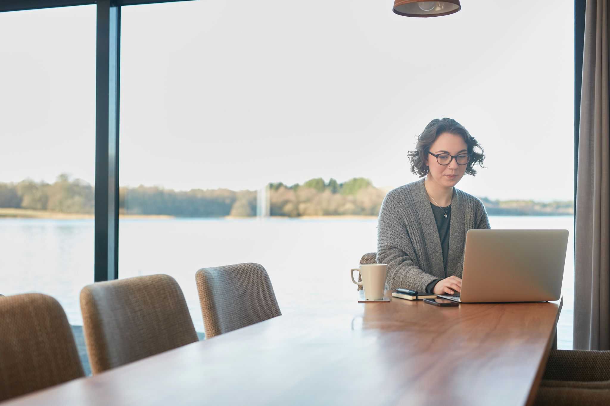 A woman sits at a dining table with a laptop