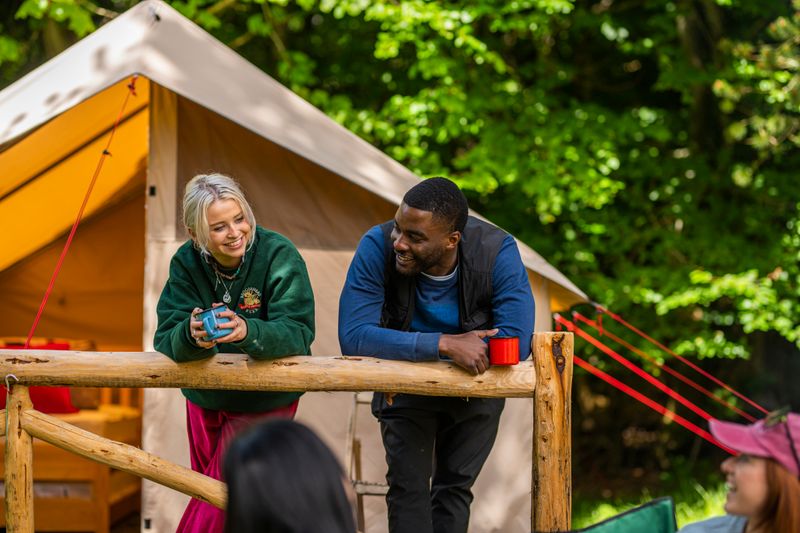 A man and women rest against railing in front of a glamping tent