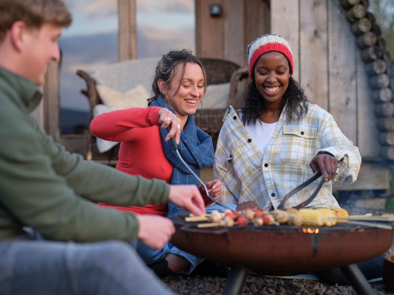 Two women and a man enjoying a meal cooking on a campfire