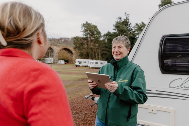 A member of staff with tablet device greets a customer beside a caravan.